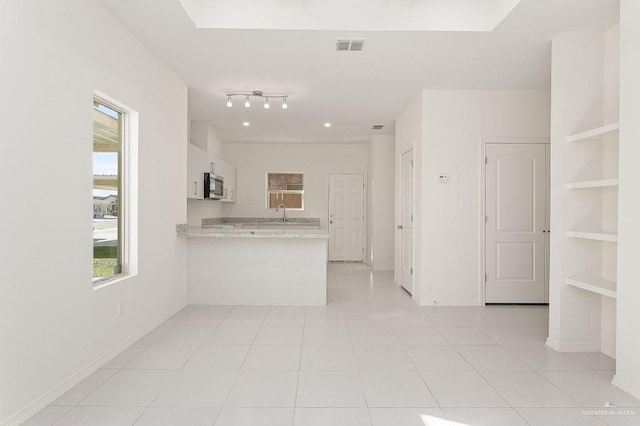 kitchen featuring stainless steel microwave, a peninsula, white cabinets, light tile patterned floors, and baseboards
