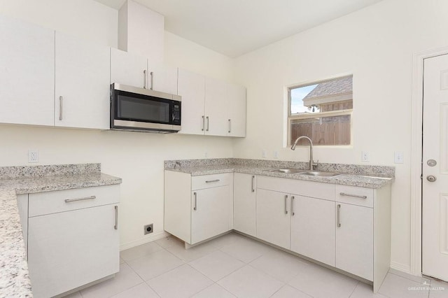 kitchen featuring stainless steel microwave, a sink, baseboards, light tile patterned floors, and light stone counters