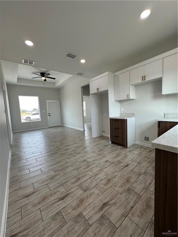 kitchen featuring a raised ceiling, white cabinetry, dark brown cabinetry, and ceiling fan