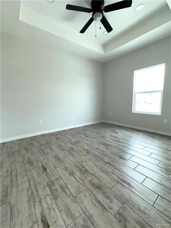 empty room featuring ceiling fan, a tray ceiling, and light hardwood / wood-style floors