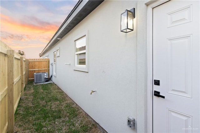 view of home's exterior with central air condition unit, stucco siding, a lawn, and fence