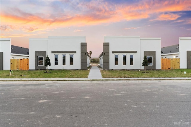 contemporary home with stucco siding, a yard, and fence