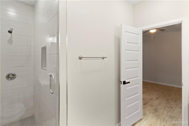 bathroom with a ceiling fan, wood finished floors, a stall shower, and baseboards