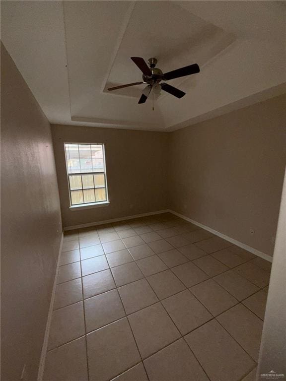 empty room featuring ceiling fan, light tile patterned flooring, and a raised ceiling