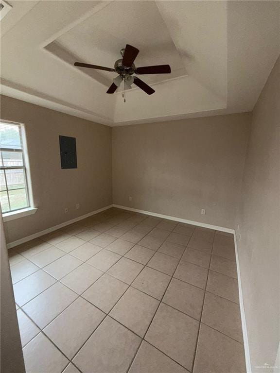 empty room with a raised ceiling, light tile patterned floors, ceiling fan, and electric panel