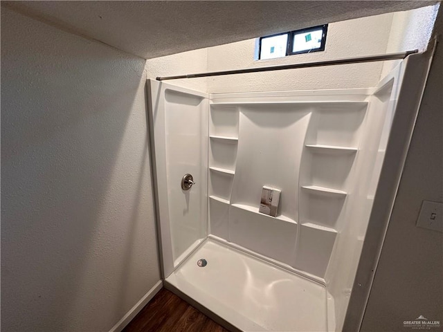 bathroom with a textured wall, walk in shower, wood finished floors, and baseboards