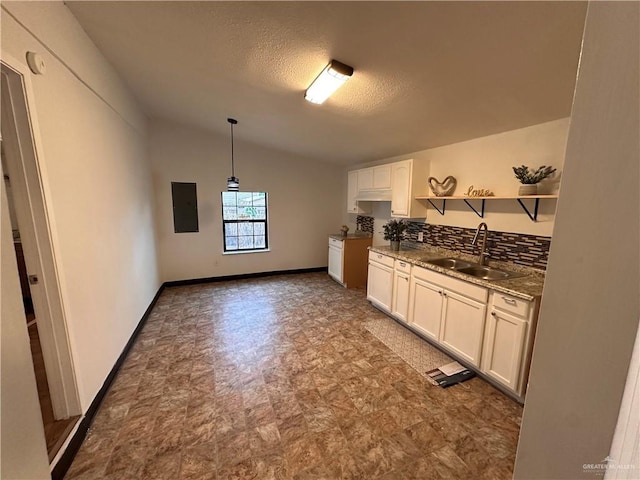 kitchen with electric panel, lofted ceiling, white cabinetry, open shelves, and a sink