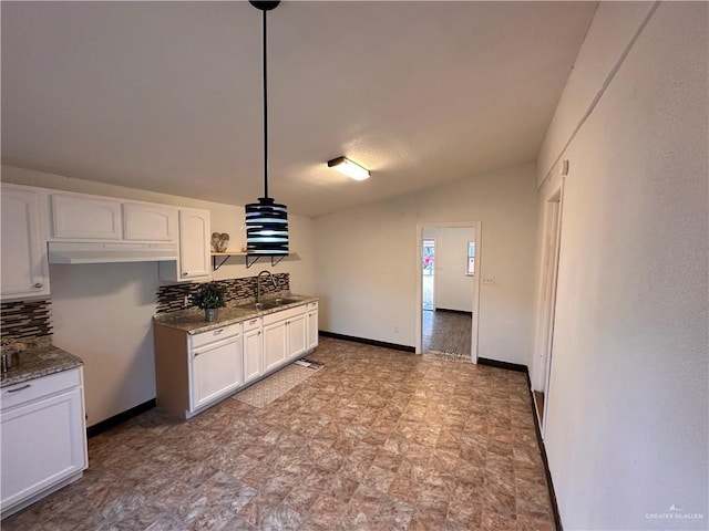 kitchen featuring light stone countertops, backsplash, white cabinets, and a sink