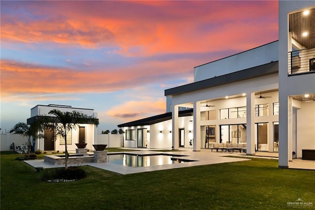 back house at dusk with ceiling fan, a yard, a patio, and an outdoor living space