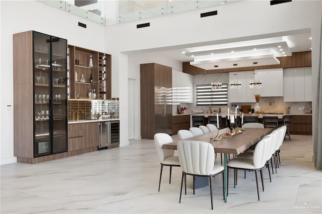 dining space with beamed ceiling, a towering ceiling, sink, and beverage cooler