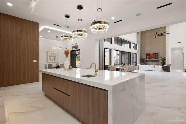 kitchen featuring sink, a large island with sink, decorative light fixtures, a fireplace, and ceiling fan with notable chandelier