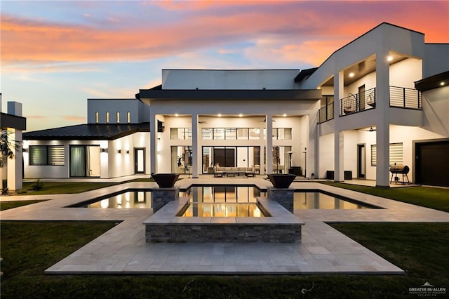 back house at dusk with an outdoor living space, a balcony, a patio, and a pool with hot tub