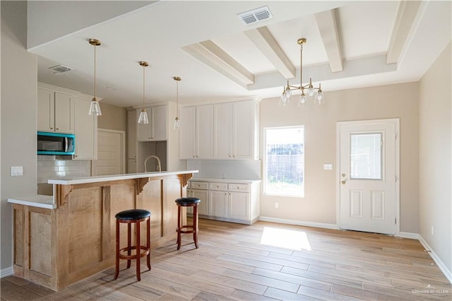 6608 Primavera St, Pharr, TX 78577 - kitchen featuring stainless steel microwave, a breakfast bar, beamed ceiling, light wood-type flooring, and white cabinetry