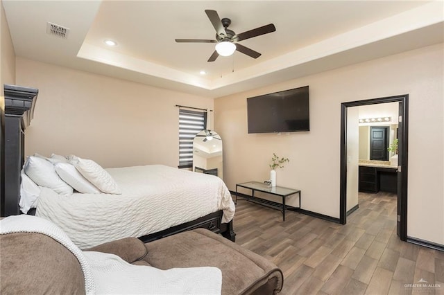 bedroom featuring hardwood / wood-style floors, ensuite bath, a raised ceiling, and ceiling fan