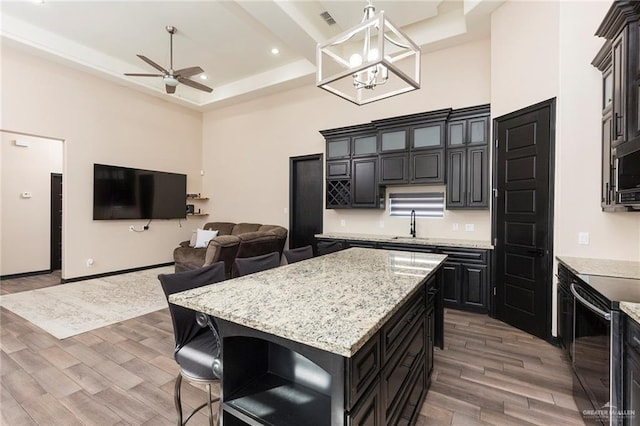 kitchen with range with electric cooktop, ceiling fan with notable chandelier, a center island, a raised ceiling, and light stone countertops