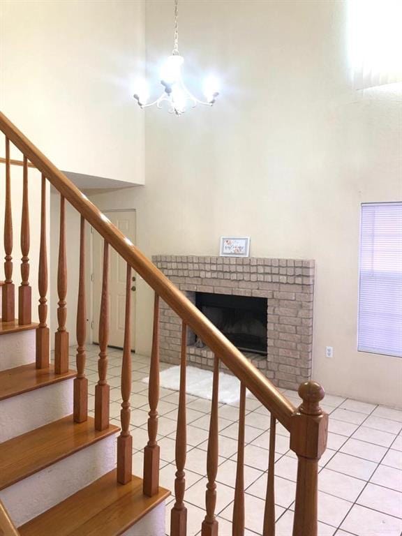 stairway with a fireplace, a towering ceiling, tile patterned flooring, and an inviting chandelier