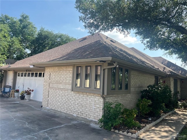 view of home's exterior featuring brick siding, a garage, roof with shingles, and concrete driveway