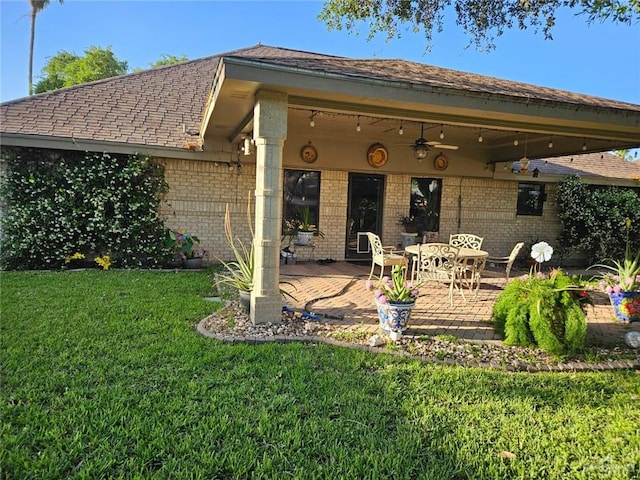 back of property with a ceiling fan, a patio area, brick siding, a yard, and a shingled roof