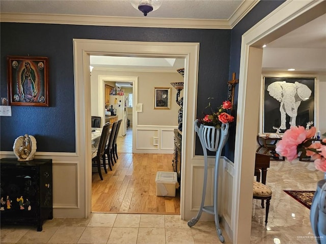 hallway with wainscoting, ornamental molding, light tile patterned flooring, and a decorative wall