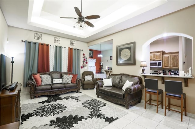 living room featuring ceiling fan, a raised ceiling, and light tile patterned floors