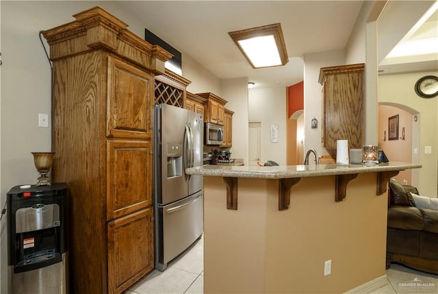 kitchen with a breakfast bar, light tile patterned flooring, kitchen peninsula, and appliances with stainless steel finishes