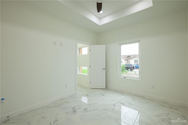 empty room with marble finish floor, a raised ceiling, and baseboards