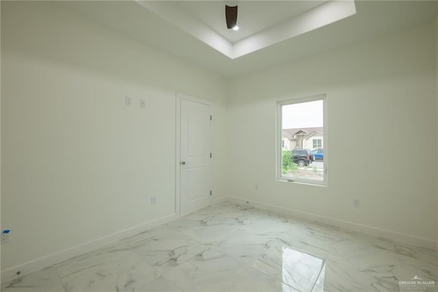 unfurnished room with marble finish floor, baseboards, and a raised ceiling