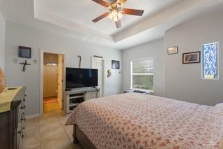 2105 Treasure Oaks Dr, Harlingen, TX 78550 - bedroom with light tile patterned floors, a tray ceiling, and a ceiling fan