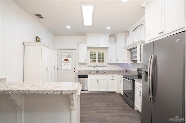 kitchen with appliances with stainless steel finishes, dark hardwood / wood-style flooring, sink, white cabinetry, and a breakfast bar area