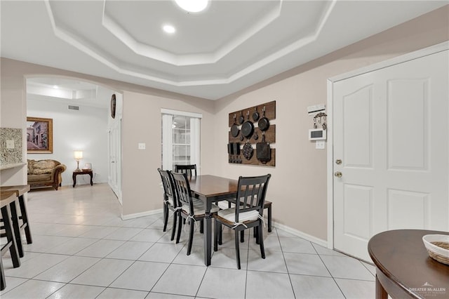 dining space with arched walkways, a tray ceiling, and light tile patterned floors