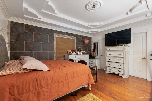 bedroom featuring ornamental molding, a tray ceiling, tile walls, and wood finished floors