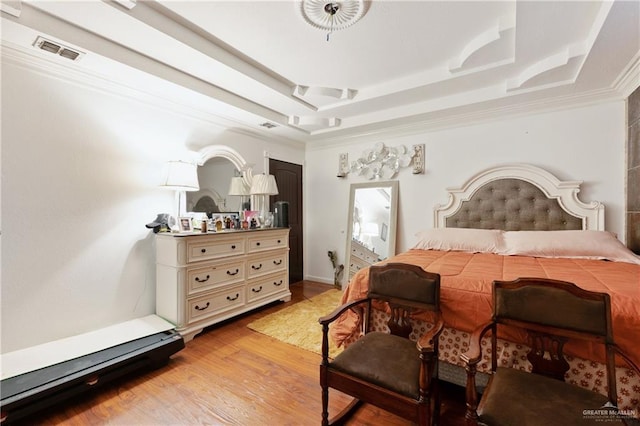 bedroom featuring light wood-type flooring, visible vents, a raised ceiling, and ornamental molding