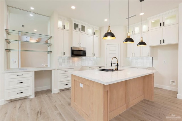 kitchen with sink, white cabinets, tasteful backsplash, light hardwood / wood-style flooring, and an island with sink