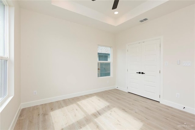 empty room with a wealth of natural light, ceiling fan, light hardwood / wood-style flooring, and a raised ceiling