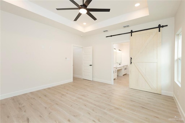 unfurnished room with sink, ceiling fan, light hardwood / wood-style floors, a barn door, and a tray ceiling