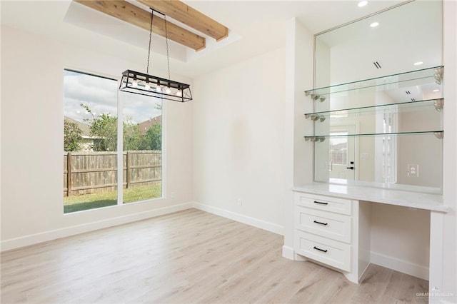 unfurnished dining area featuring built in desk, light hardwood / wood-style flooring, and beamed ceiling