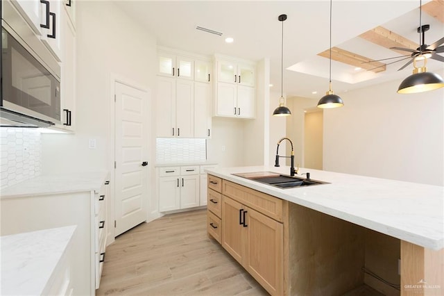 kitchen featuring sink, light wood-type flooring, backsplash, hanging light fixtures, and a center island with sink