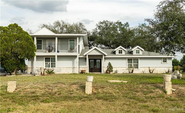 view of front facade featuring a front yard, a balcony, stucco siding, french doors, and stone siding