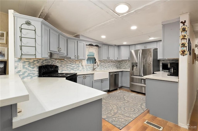 kitchen featuring gray cabinetry, light hardwood / wood-style flooring, decorative backsplash, kitchen peninsula, and stainless steel appliances