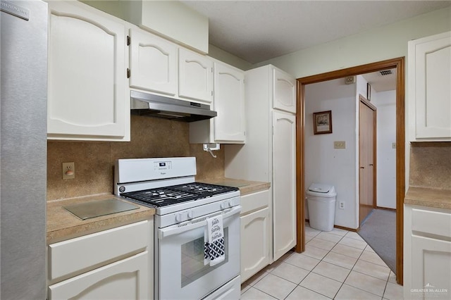 kitchen featuring white gas range, decorative backsplash, white cabinets, and light tile patterned floors