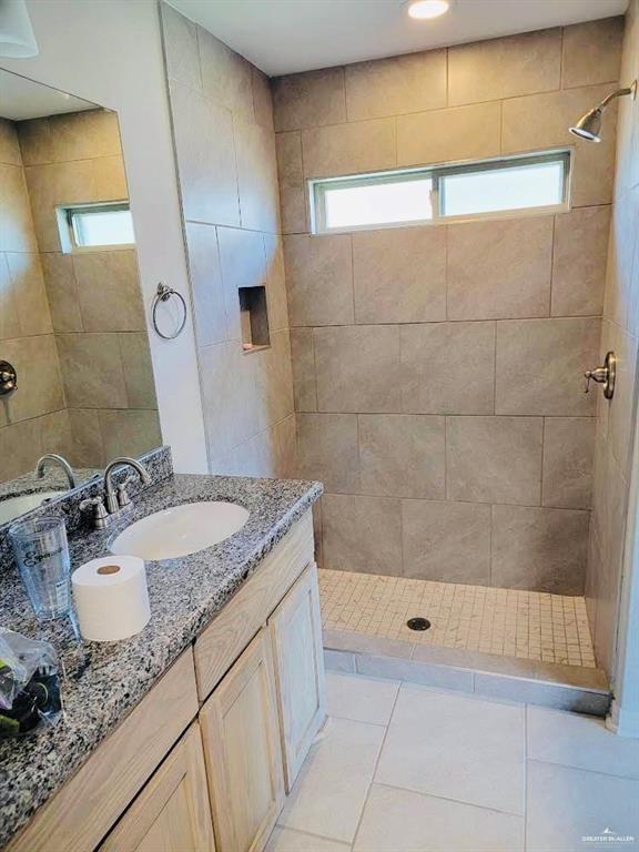 bathroom featuring tile patterned flooring, a tile shower, vanity, and a wealth of natural light