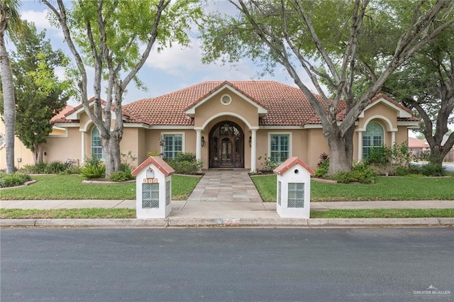 mediterranean / spanish home with a front lawn, stucco siding, and a tiled roof