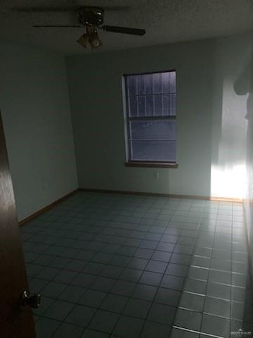 tiled empty room featuring ceiling fan and a textured ceiling