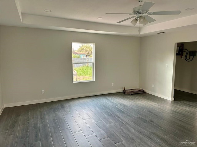 empty room with a tray ceiling, ceiling fan, and dark hardwood / wood-style floors