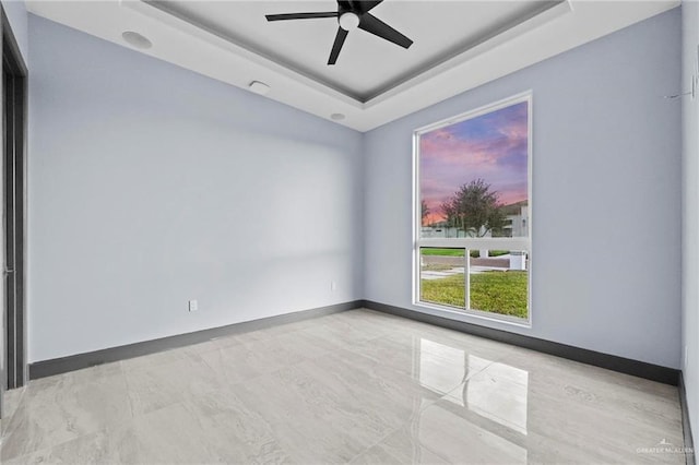 spare room with ceiling fan and a raised ceiling