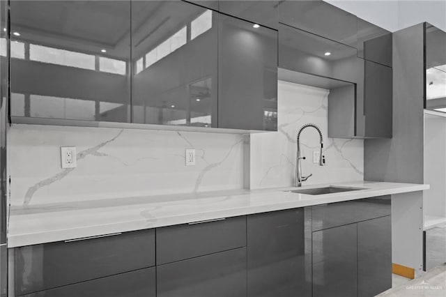 kitchen with light stone counters, sink, tasteful backsplash, and gray cabinetry