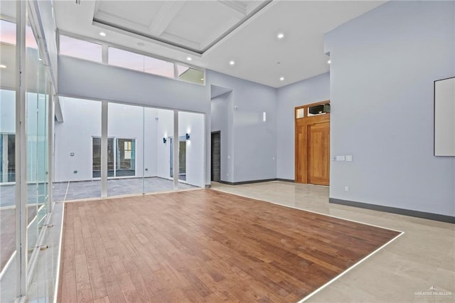 unfurnished living room featuring a towering ceiling, coffered ceiling, and light hardwood / wood-style floors