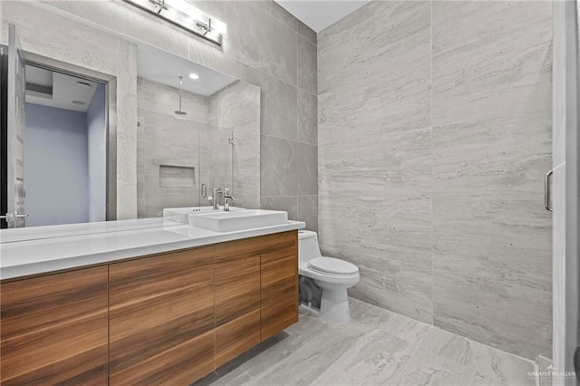 bathroom with vanity, toilet, a shower with door, and tile walls