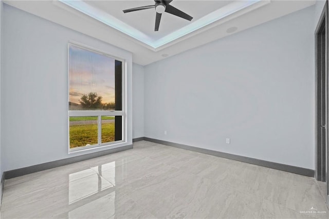 empty room with ceiling fan and a tray ceiling