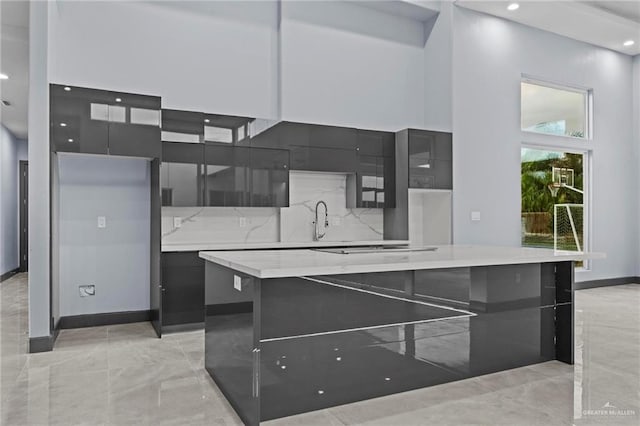 kitchen featuring sink, tasteful backsplash, black electric cooktop, a kitchen island, and a towering ceiling